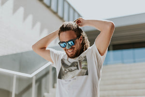 Young, casually dressed man descending outdoor stairs, adjusting his long hair. Blue Nöz protects his nose stylishly.